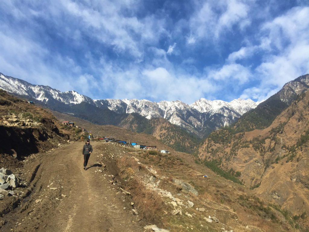 Tamang Heritage trekking – trekker wandelt weg van een dorp met zicht op de Himalayas
